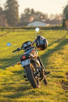 Classic motorcycle parked in a lush green field during golden hour, offering a serene outdoor setting.