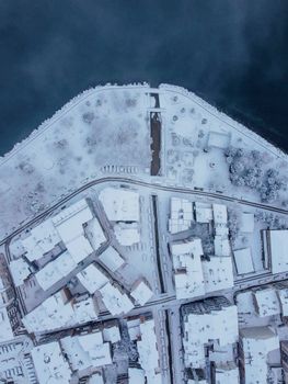 Drone shot of a snow-covered Turkish city beside a body of water in winter.