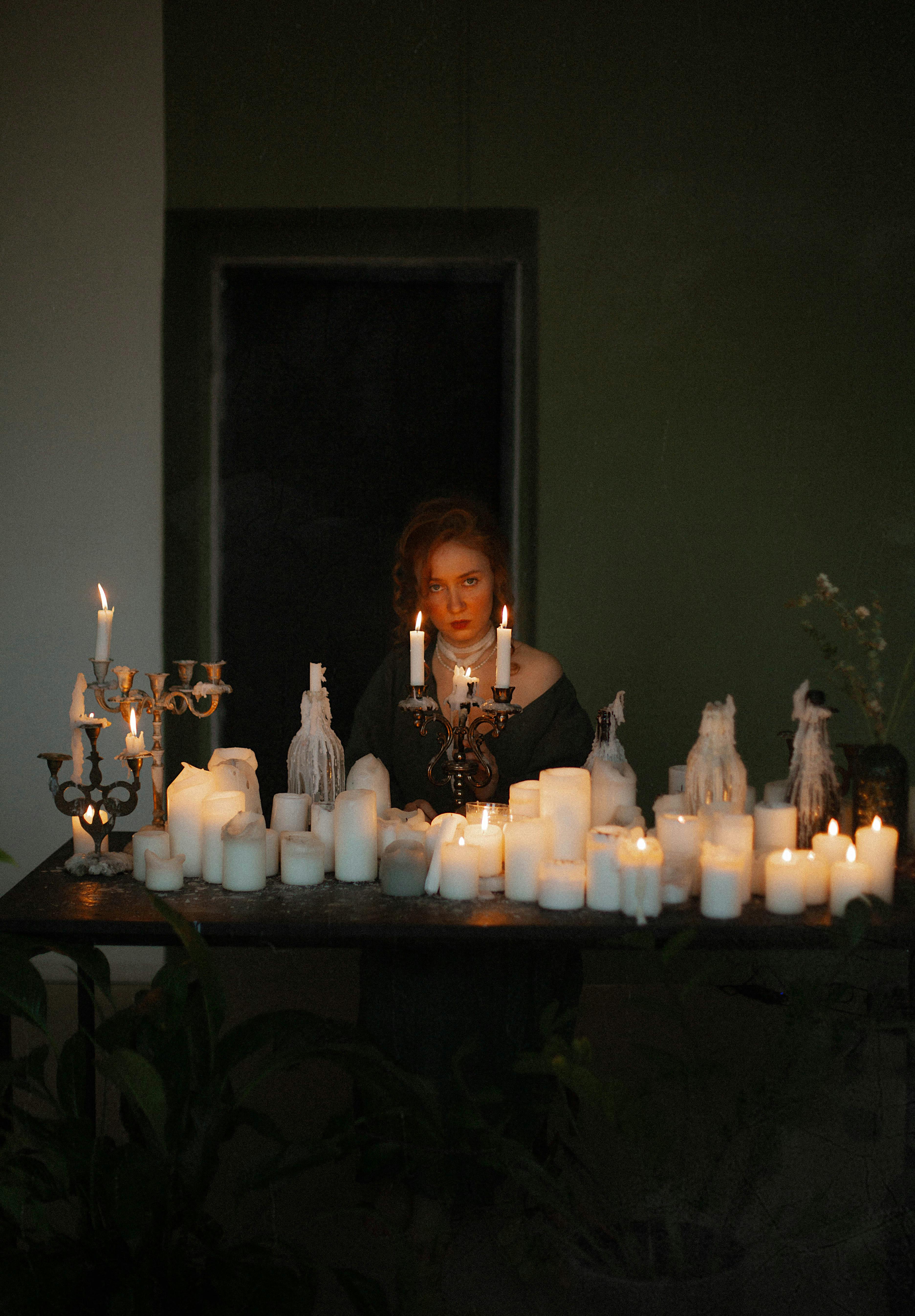 A woman surrounded by candles creates an atmospheric scene in a dimly lit room, capturing a mysterious mood.