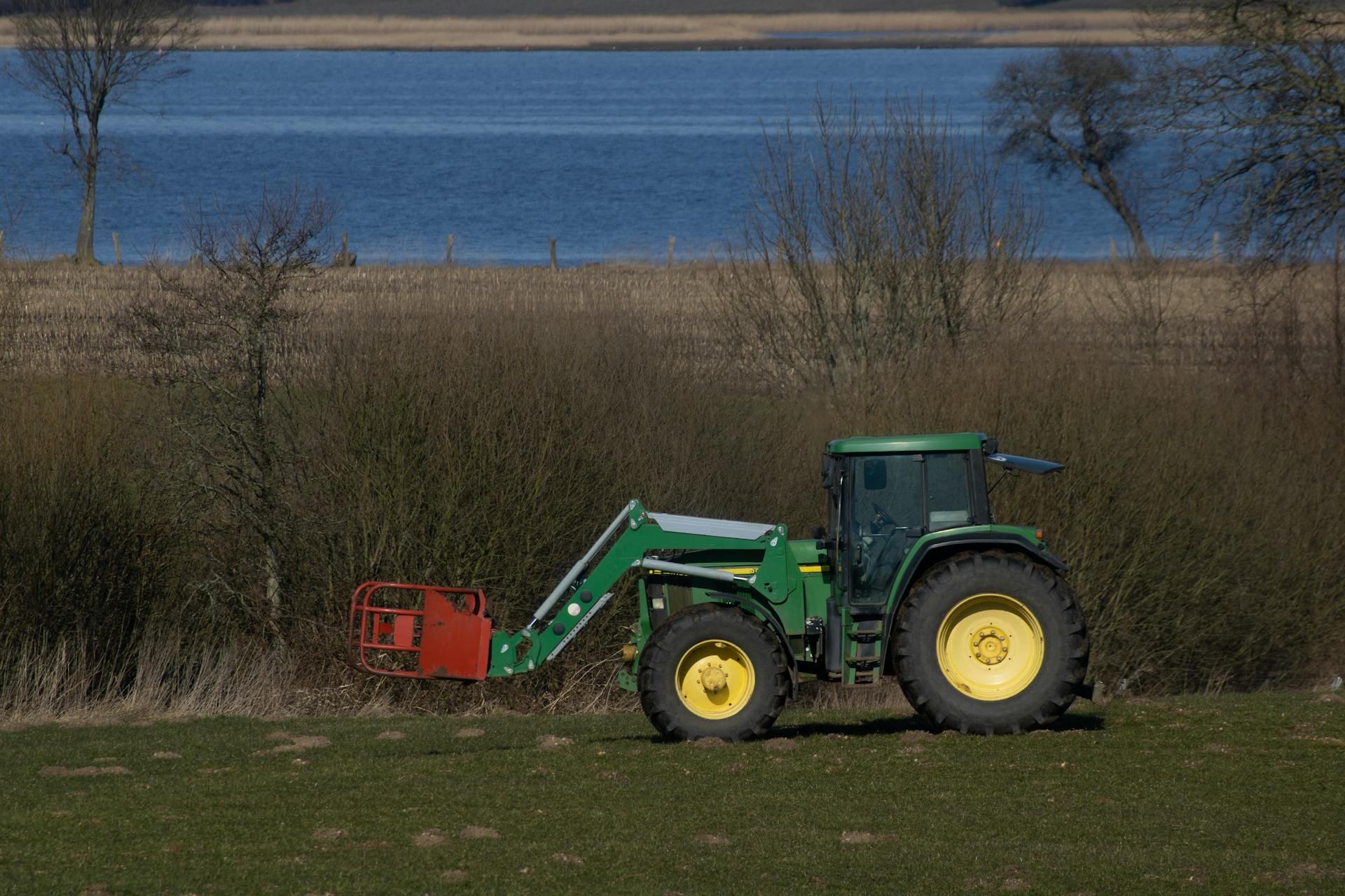 A Green Tractor with Red  Loader on Green Grass Near Lake