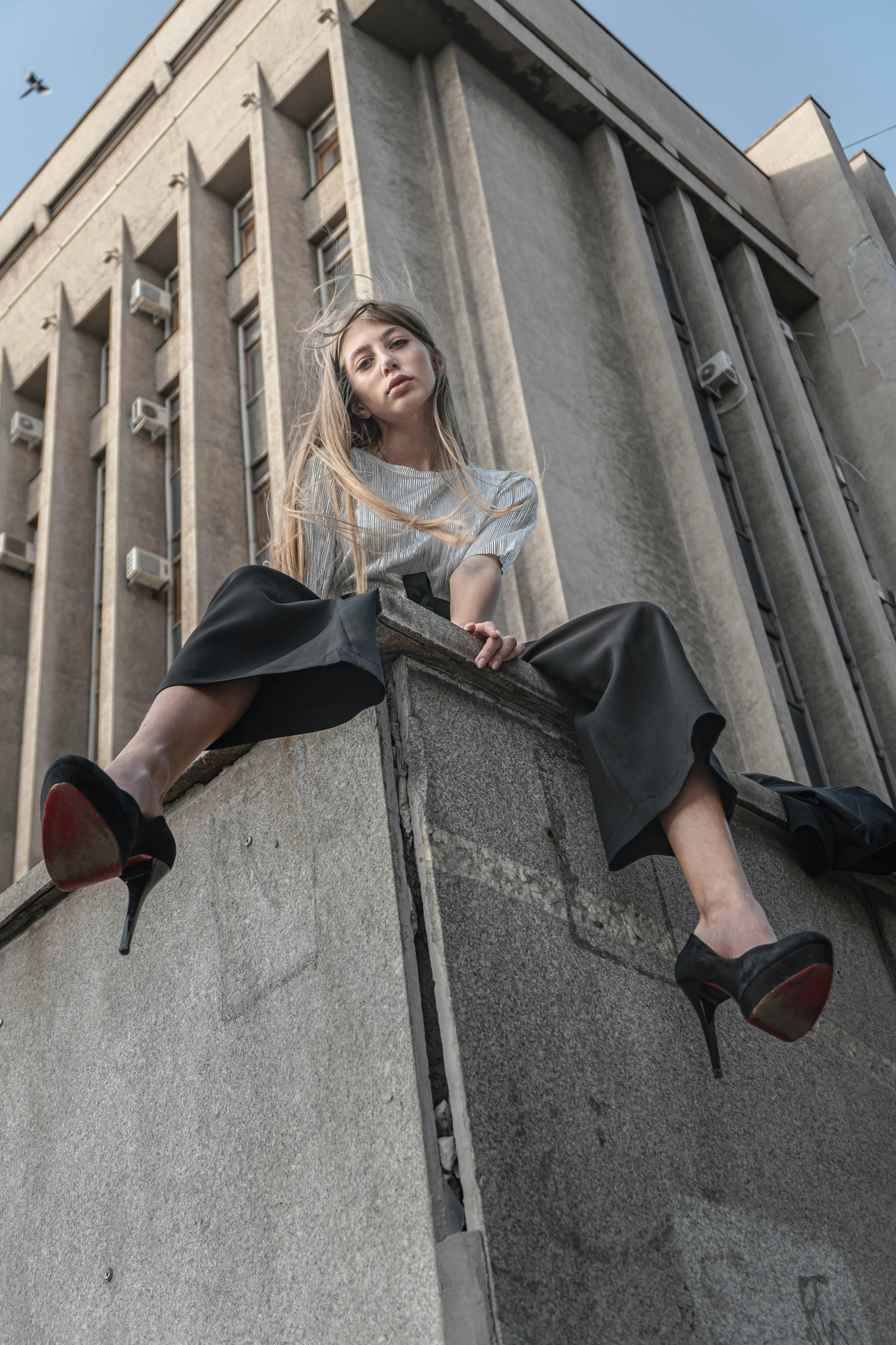 A Woman Wearing High Heels Sitting on the Concrete Structure Near the