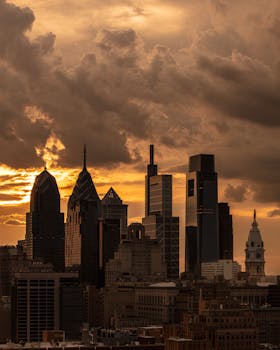Dramatic sunset over Philadelphia skyline with iconic skyscrapers silhouetted against a cloudy sky.
