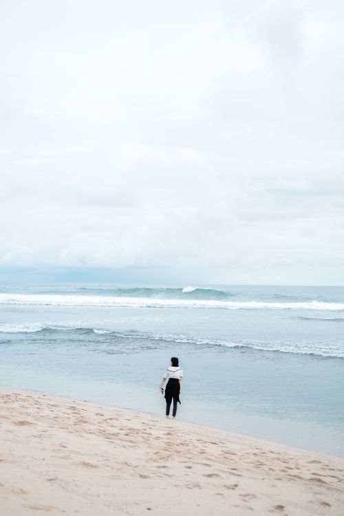 Free Person standing alone on Kretek Beach, Indonesia, embracing solitude and nature. Stock Photo
