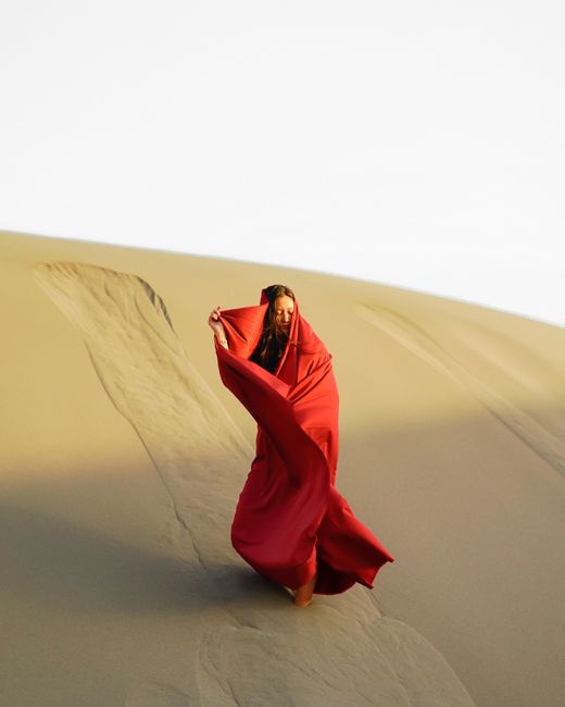 A woman wrapped in red fabric stands on a sand dune in Jogja, Indonesia.