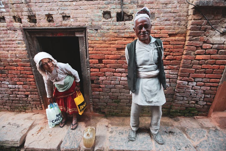 Elderly Man And Woman Standing Outside Of A Brick House