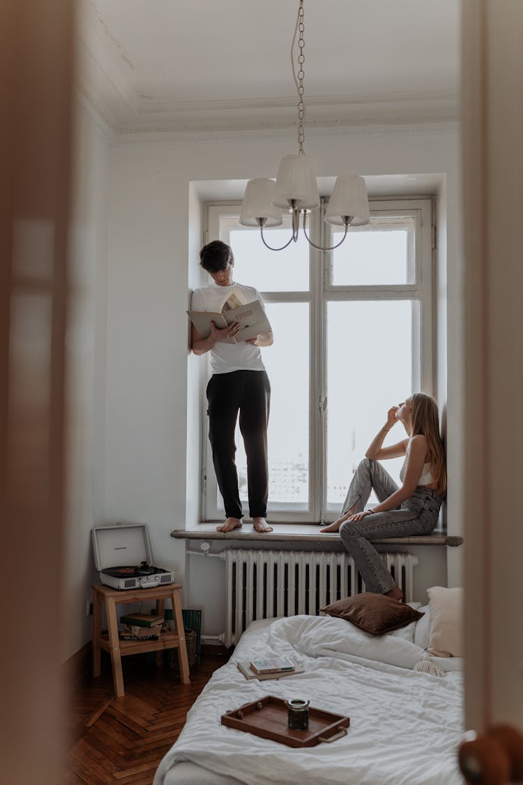 Young Man Standing On Windowsill And Woman Sitting On Windowsill