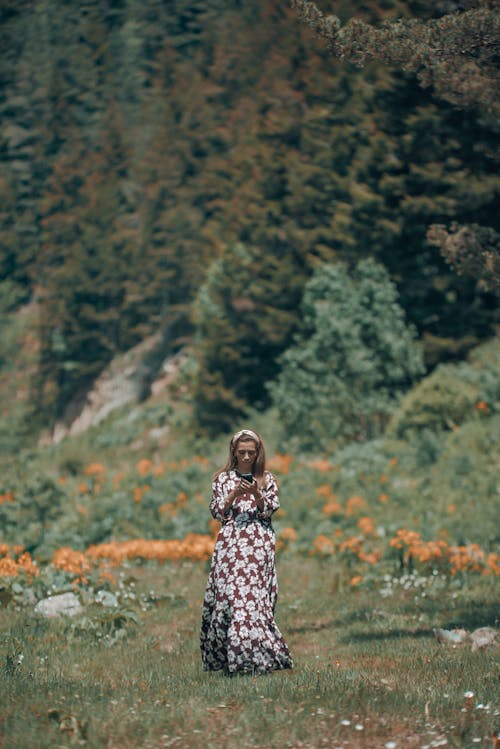 Free Woman in Black and White Floral Dress Standing on Green Grass Field Stock Photo