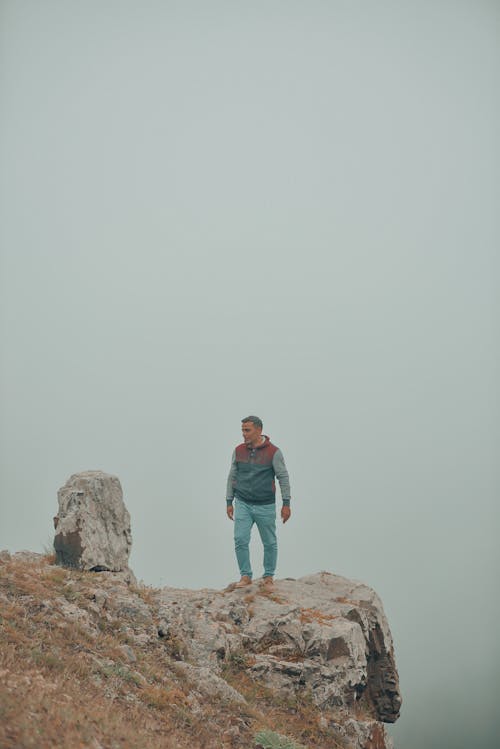 Free A Man Standing on the Rock Formation Under Gray Sky Stock Photo