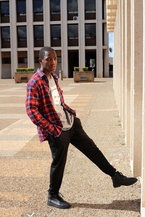 Free African man with hands in pockets leaning on a wall in Bulawayo. Stock Photo