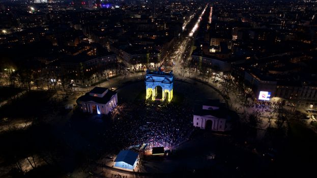 Stunning aerial view of a historical arch illuminated at night in a bustling cityscape.