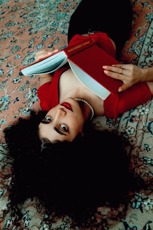 A Woman Lying on the Floral Carpet Reading a Book