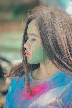 Close-up of a young woman with vibrant colors on her face, celebrating the Holi festival outdoors.