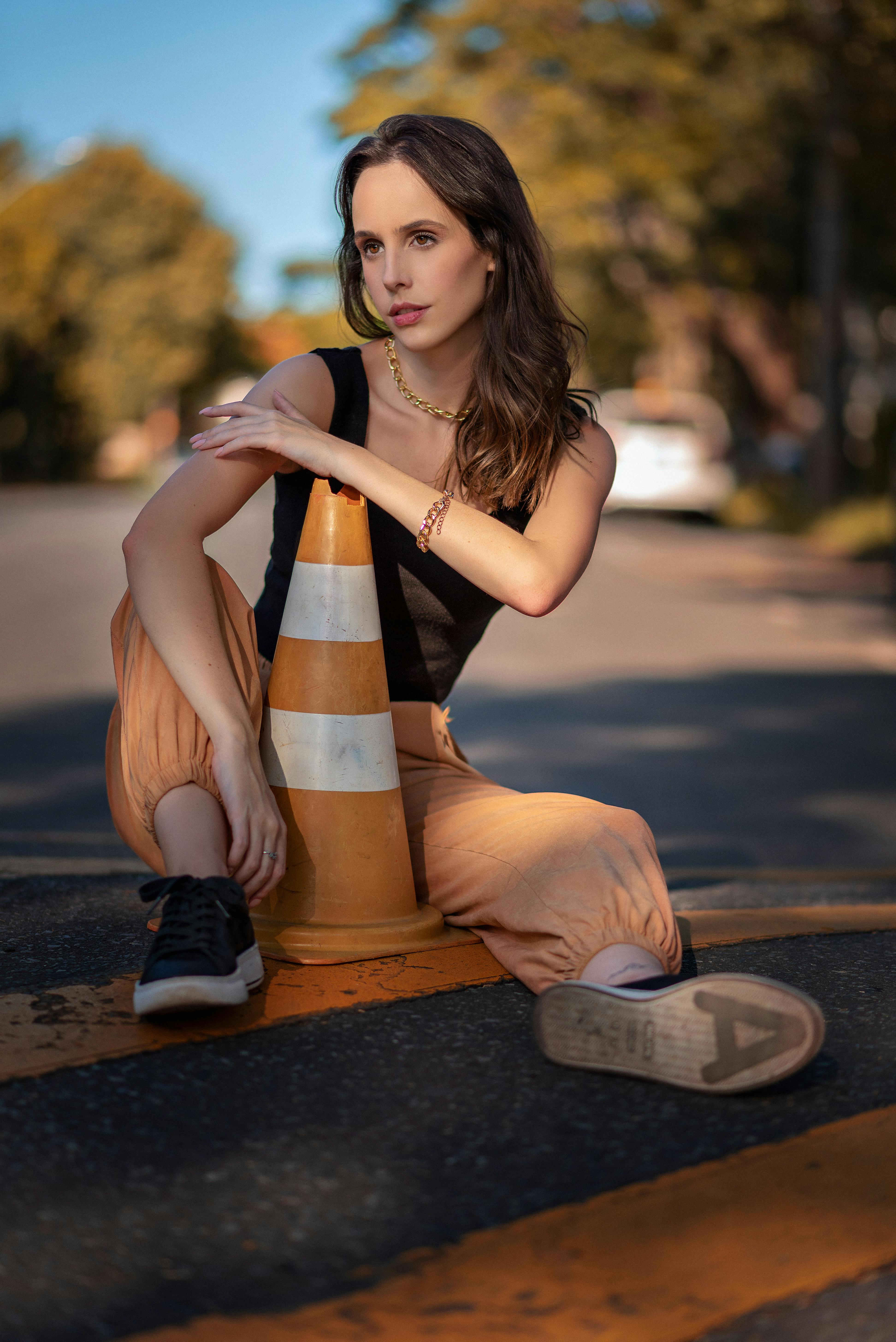 a woman in black top and pants holding a traffic cone sitting on a road