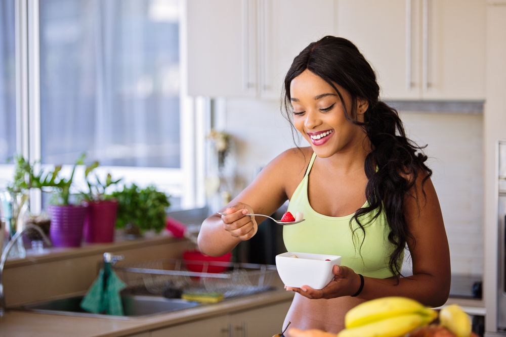 Femme souriante dégustant un bol de fruits frais et colorés dans une cuisine lumineuse