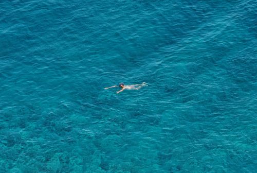Free Aerial shot of a lone swimmer in the stunning turquoise waters of Greece. Stock Photo