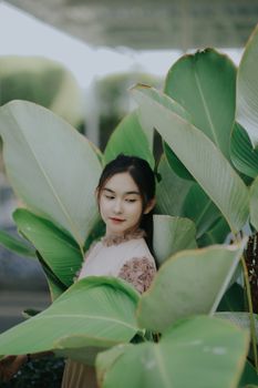 Portrait of a serene young woman nestled among large tropical leaves in a soft, natural setting.