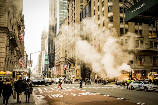 Busy urban street scene in New York City with pedestrians, traffic, and steam rising from manholes.