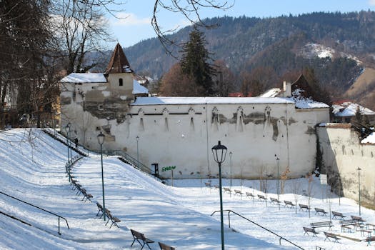 A snowy winter scene at Weaver Bastion in Brasov with benches and fortress walls.