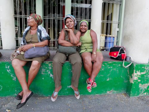 Free Three women sitting on a concrete bench, smiling and relaxing outdoors. Stock Photo
