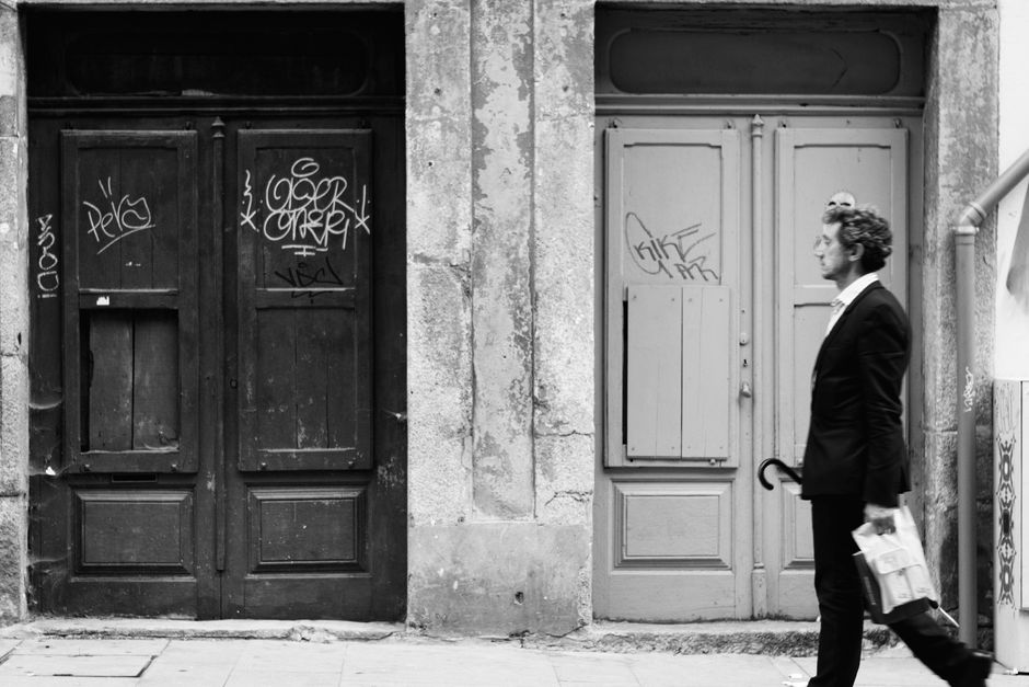 Black and white photo of a man walking past graffitied wooden doors.