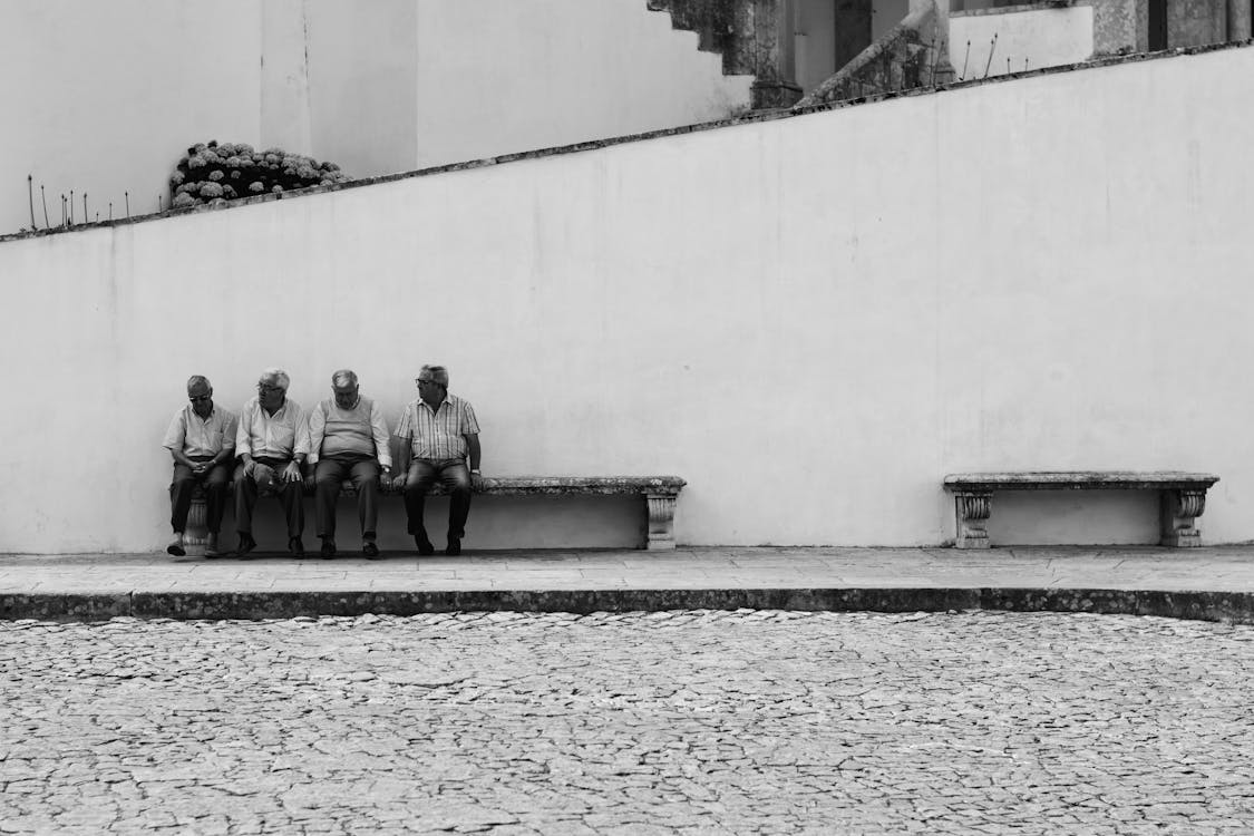 Grijswaardenfoto Van Vier Mannen Zittend Op Een Bankje Langs De Straat