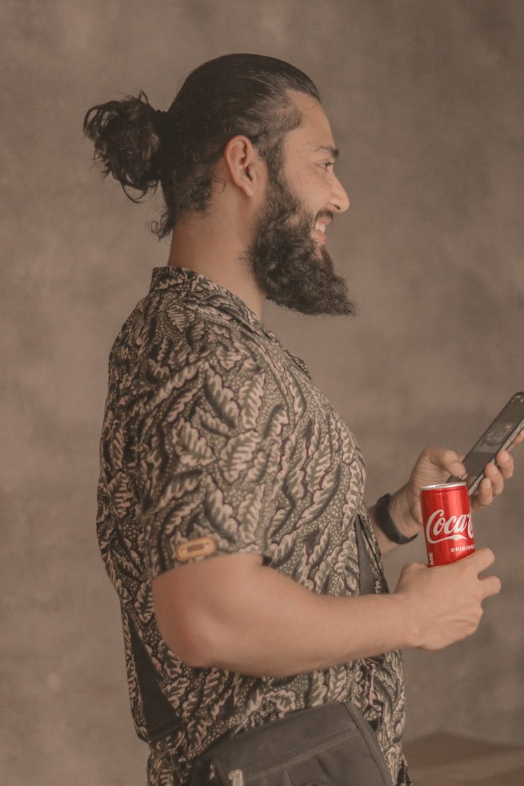 A Bearded Man In Ponytail Holding A Smartphone And A Can Of Softdrink