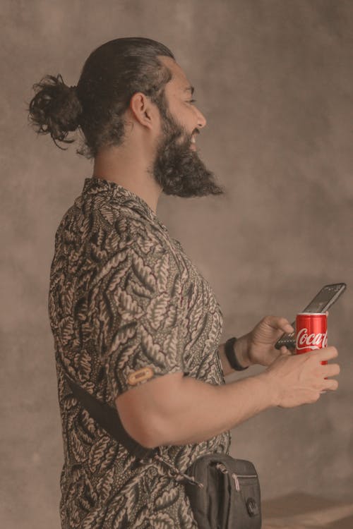 A Bearded Man Holding a Soda Can and a Smartphone