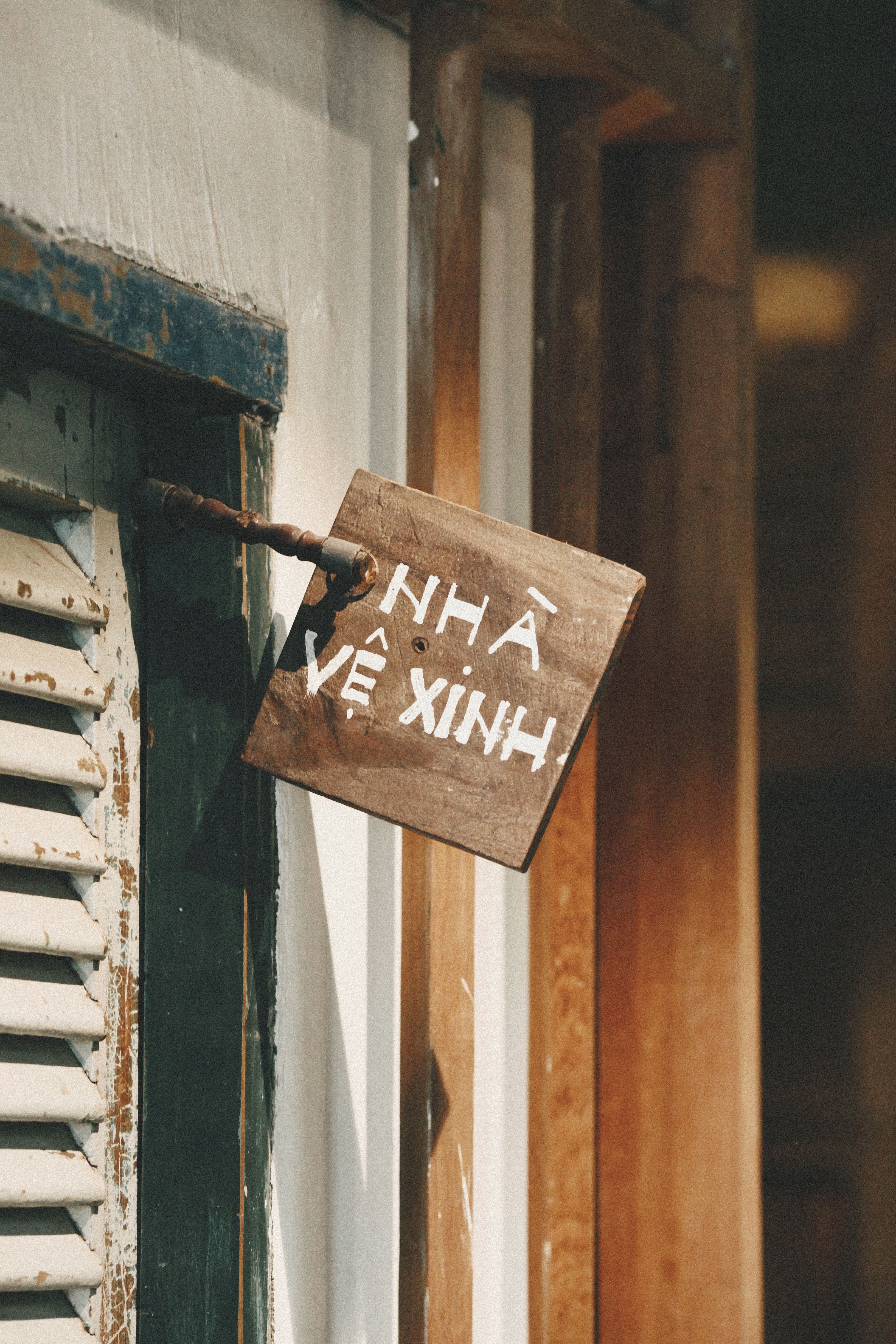 Wooden sign with Vietnamese text hanging on a rustic exterior wall.