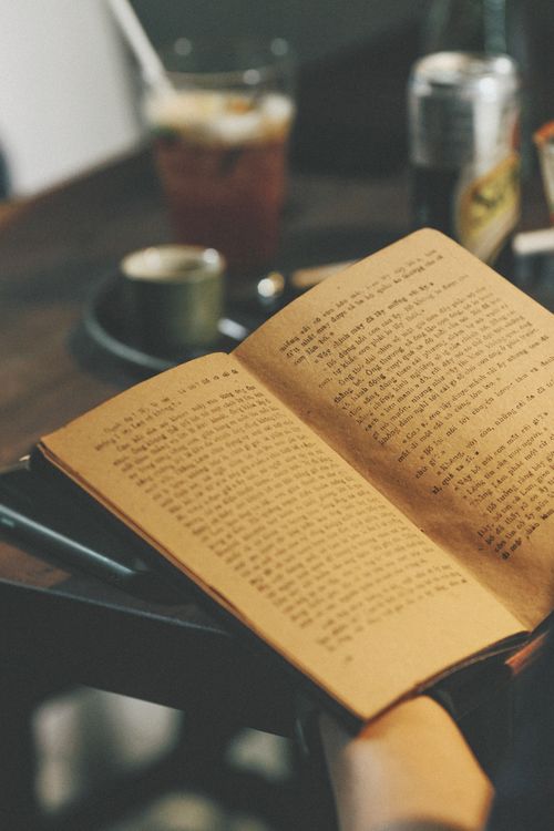 Free A close-up of an open book in a cozy, vintage setting with a coffee cup in the background. Stock Photo