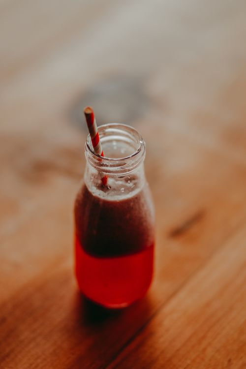 Free A refreshing berry juice in a glass bottle with a straw on a wooden table. Stock Photo