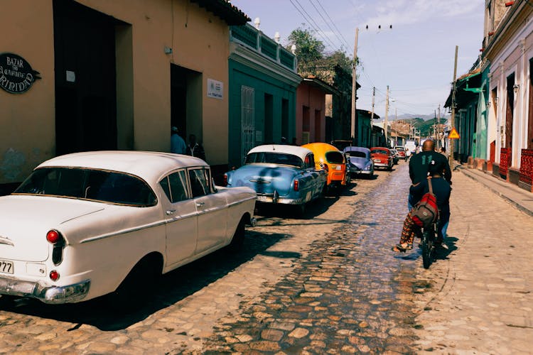 Man Riding Bicycle Past Row Of Vintage Car Parked By Street