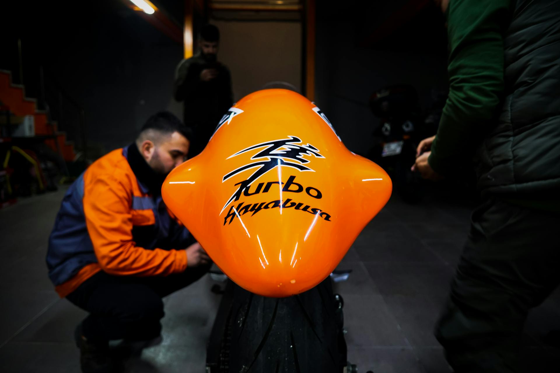 A group of mechanics working on a shiny orange turbo motorcycle in a dimly lit garage setting.