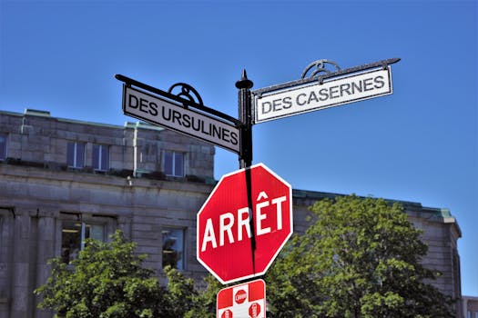Bilingual street signs with stop sign against a clear blue sky in a city setting, featuring historical street names.