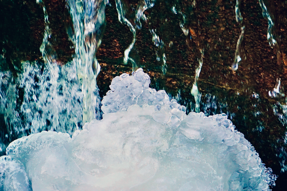 Close-up of a frosty waterfall flowing over icy, textured surfaces in winter.