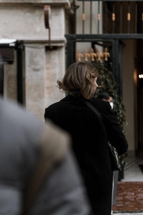 Free Woman in a black coat walking past a building entrance outdoors, capturing an everyday urban scene. Stock Photo