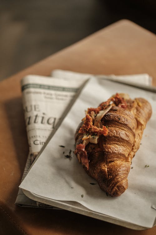 Free Croissant on Newspaper Lying on Table Stock Photo