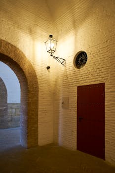 Warm light on an archway and red door in Seville, Spain, showcasing Moorish architecture.