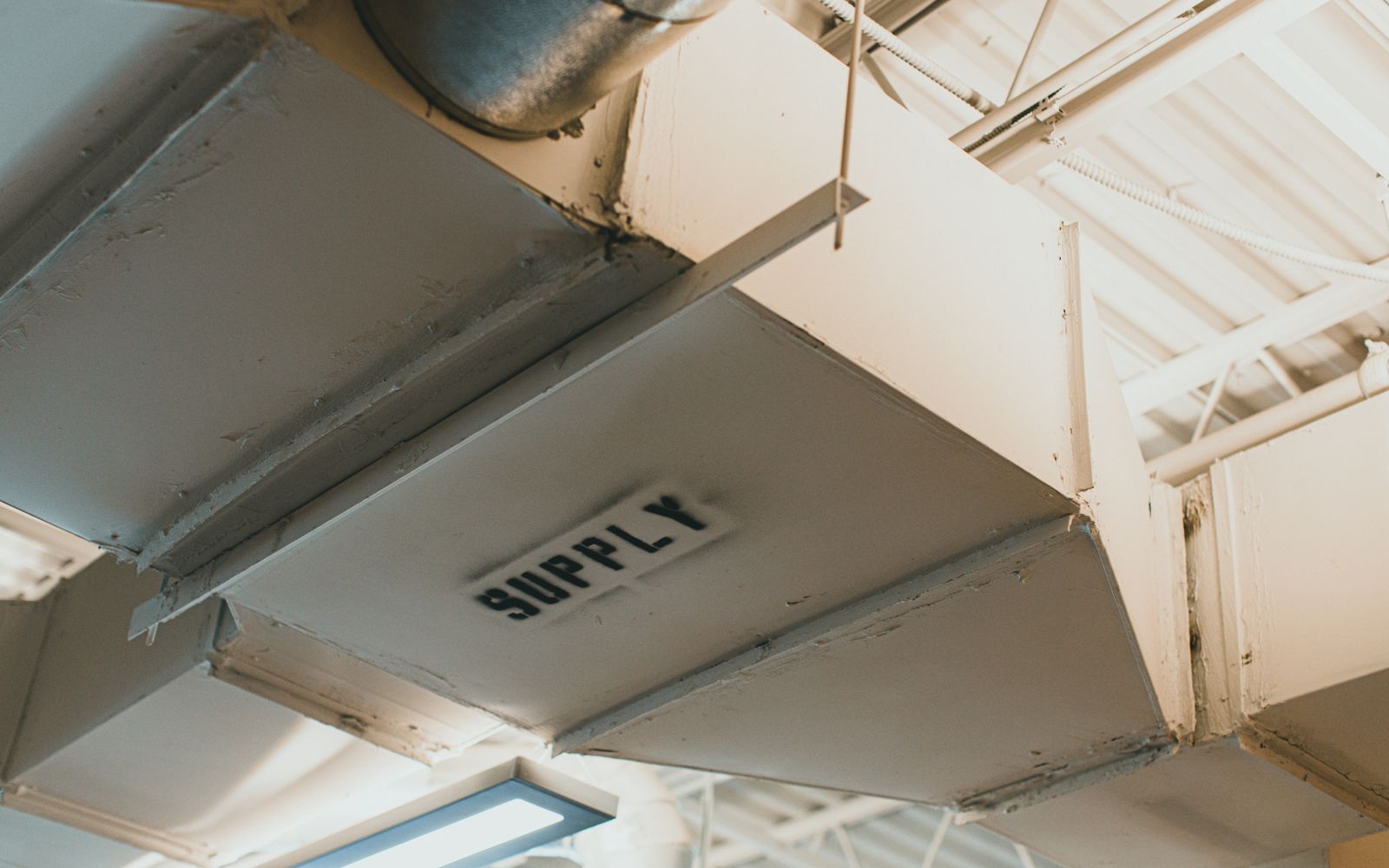 Close-up of a white metal HVAC supply air duct against a neutral wall
