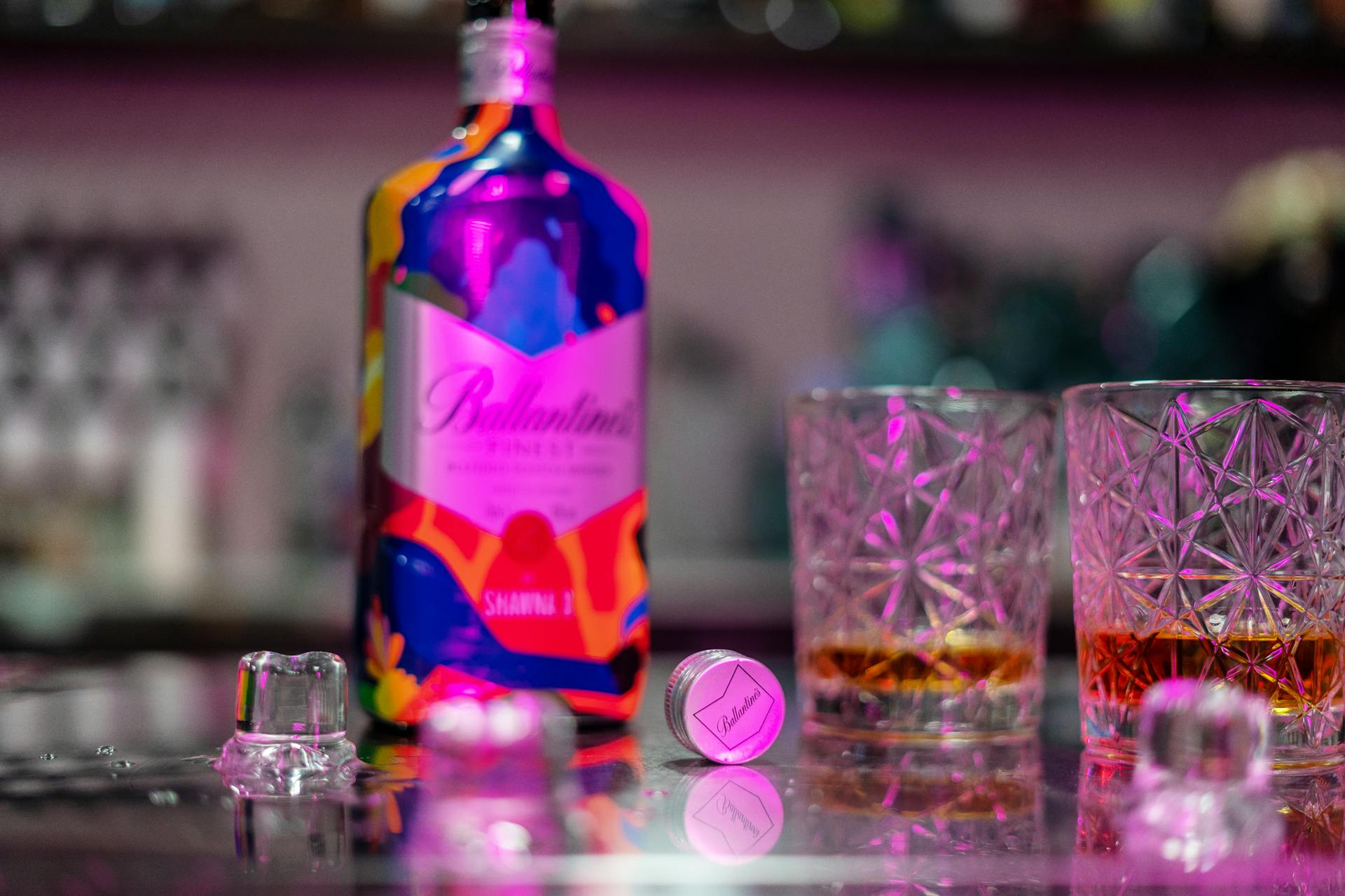 A vibrant Ballantine's bottle with whiskey in elegant crystal glasses on a reflective surface.