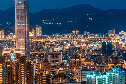 A breathtaking aerial view of a city skyline at night with illuminated skyscrapers and mountains in the background.