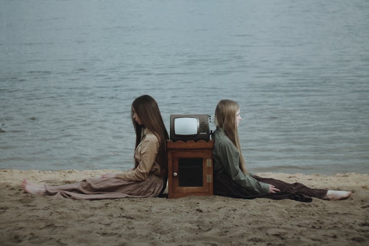 Girls Sitting Back To Back On Beach