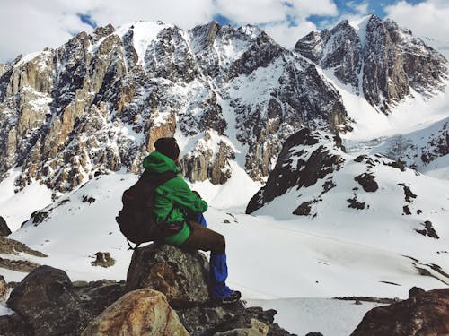 A Man Sitting on a Rock with a View of Snow Covered Mountains