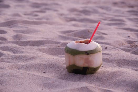 Refreshing coconut drink with straw on sandy beach during sunset, perfect tropical getaway vibe.