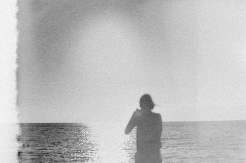 Free A silhouetted person stands by the sea during sunset, creating a calm and serene atmosphere. Stock Photo