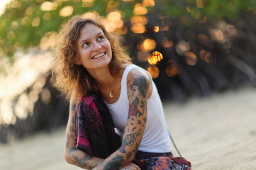 Free A joyful woman with tattoos sits outdoors, smiling in a relaxed, nature-filled setting. Stock Photo