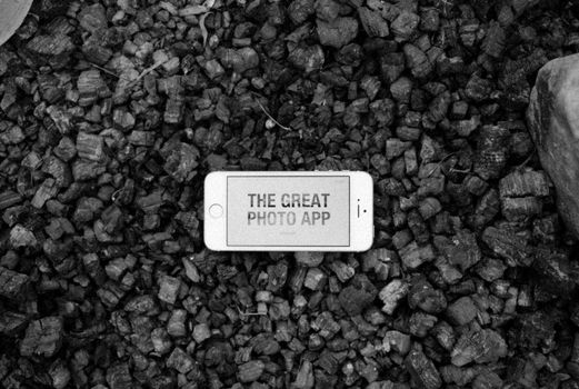 Black and white image of a smartphone displaying 'The Great Photo App' on gravel.