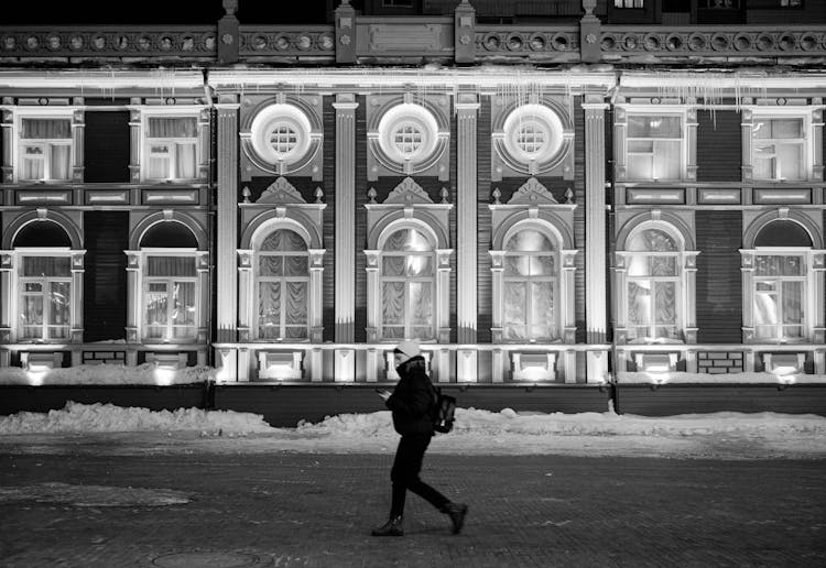 A Grayscale Of A Woman In Winter Clothing Walking While Texting