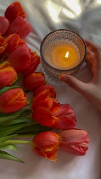A warm scene featuring red tulips next to a lit candle, evoking a cozy atmosphere.