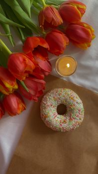 Aesthetic flat lay of a sprinkled donut, vibrant orange tulips, and a candle.