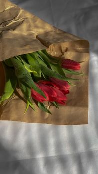 Vibrant red tulips in a rustic parchment wrap with dewdrops, captured in soft light for a fresh feel.